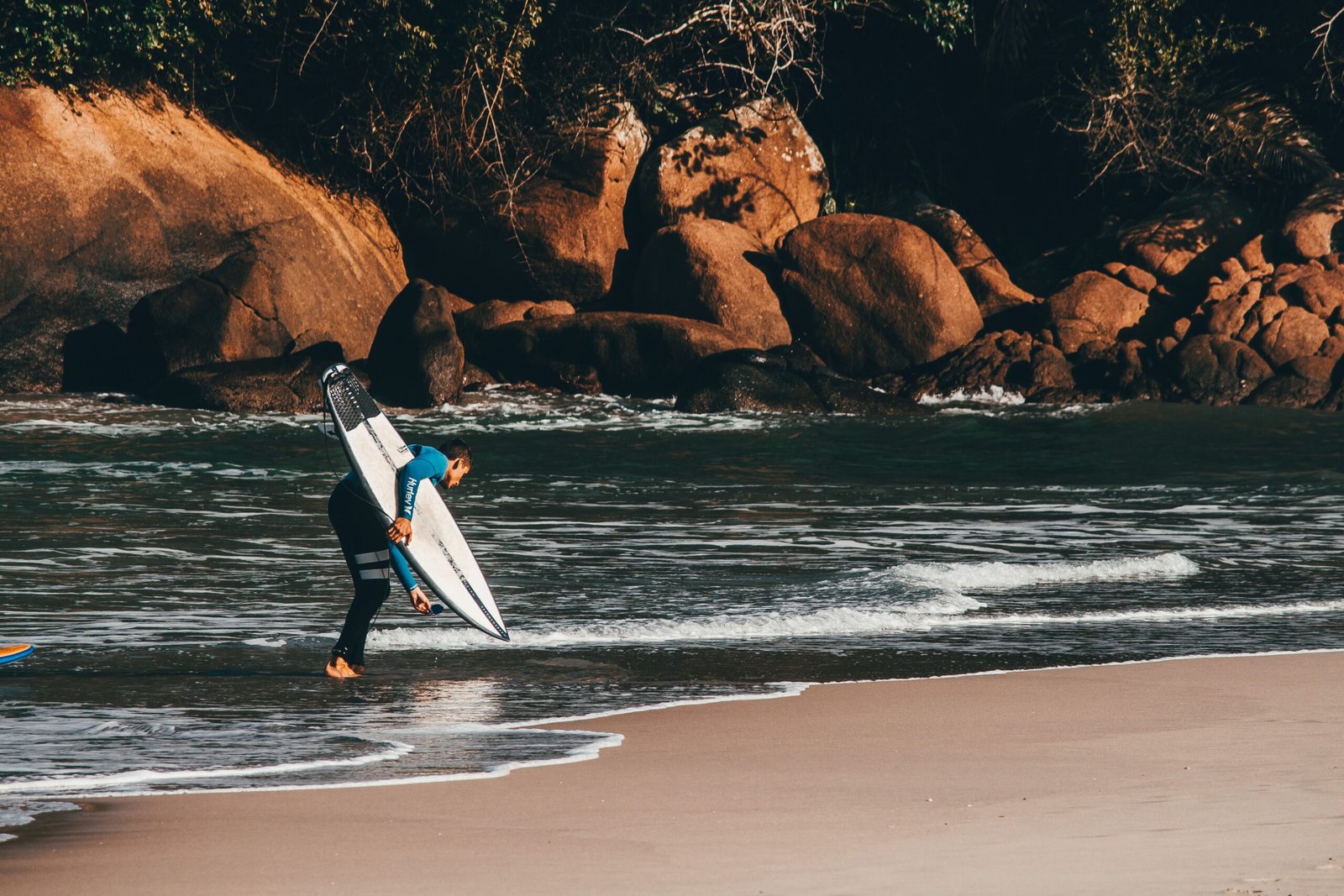 Surfer in a wetsuit standing in foamy water beside rocky headland formations