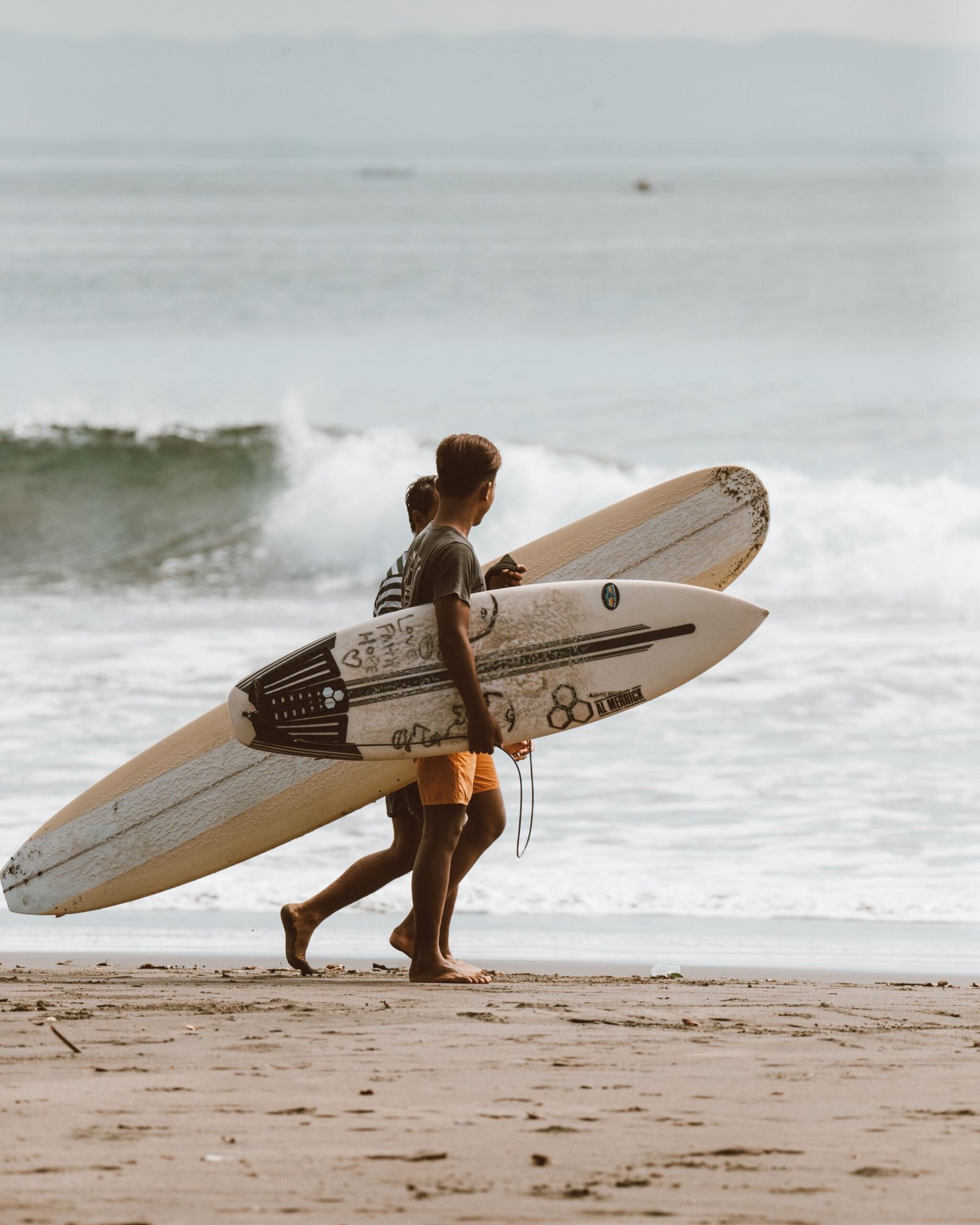 Two surfers walking along a sandy beach carrying their surfboards towards the waves