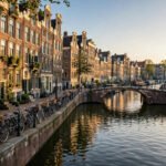A canal in Amsterdam lined with tall gabled houses and bicycles, with a bridge crossing the water.